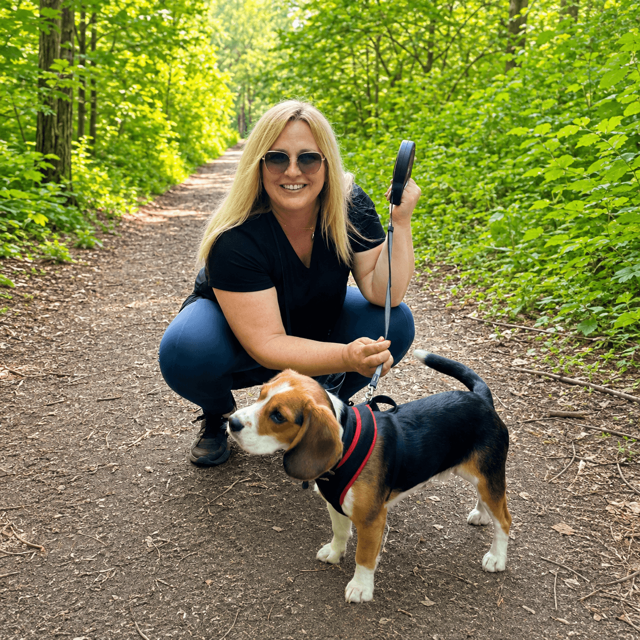 Nadia crouching beside a beagle on a woodland walk